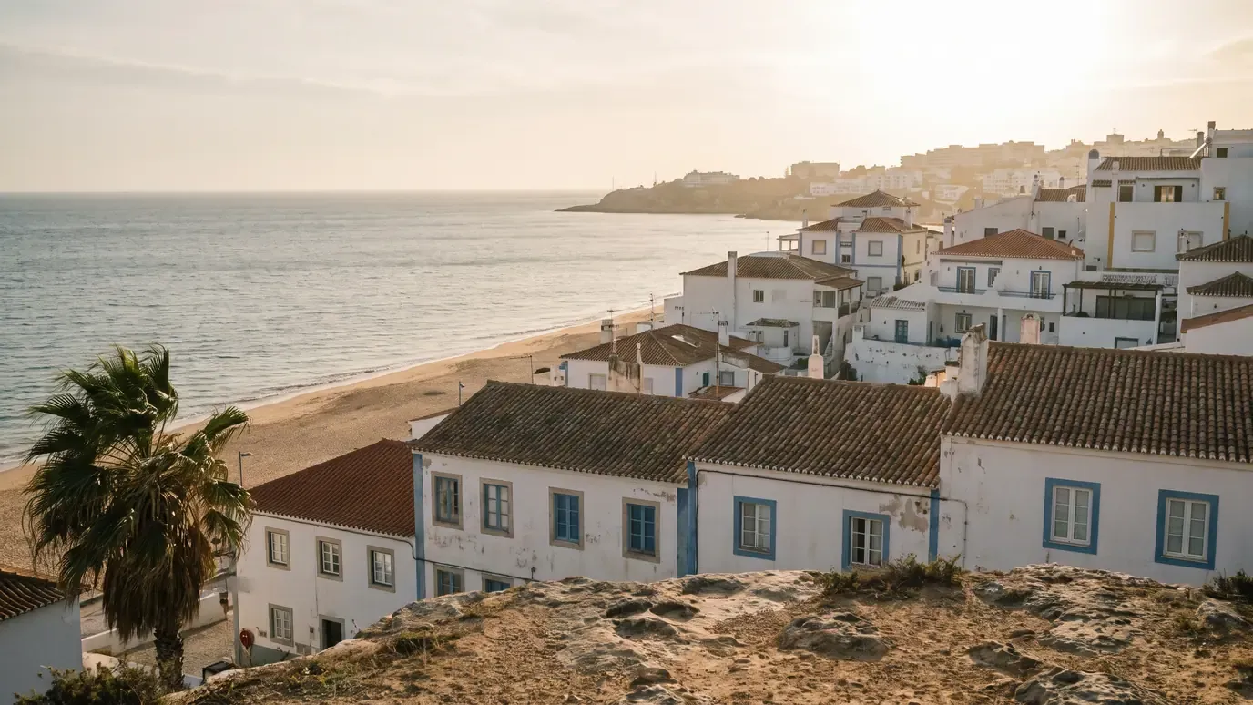 Whitewashed houses with terracotta roofs and blue window frames stepping down to the beach at Albufeira, with the sea behind