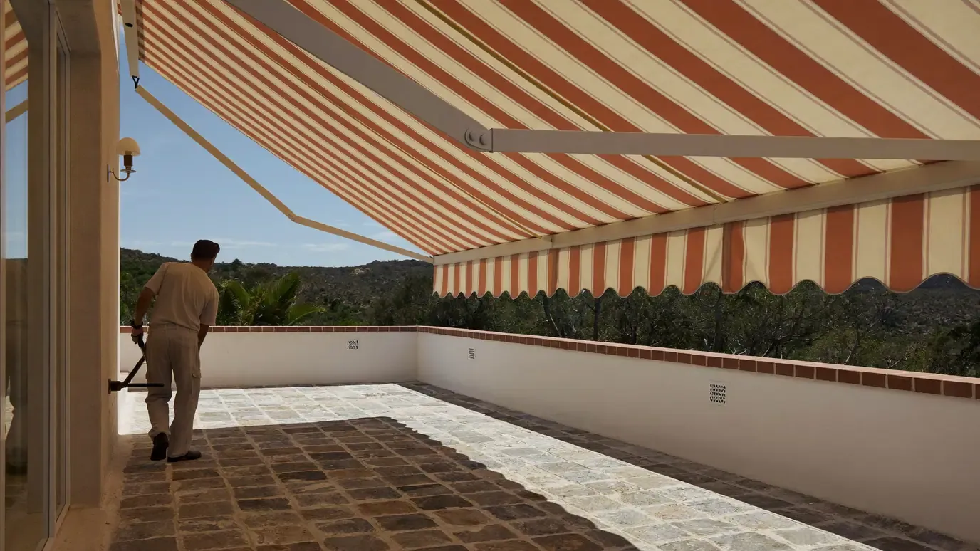 Striped folding arm awning extended over a villa terrace, being wound out with a crank handle