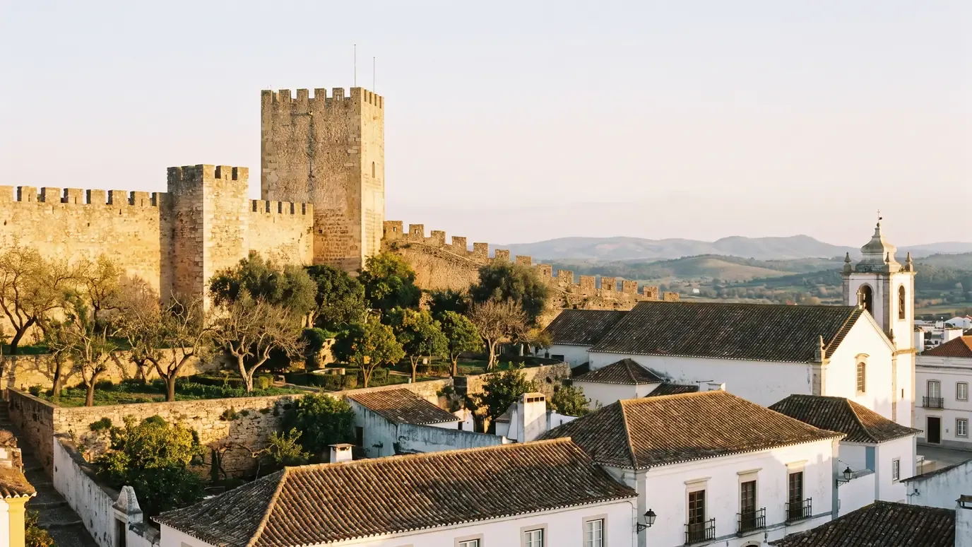 The medieval castle walls and tower of Loulé above a garden of orange trees, with a church tower and terracotta roofs behind