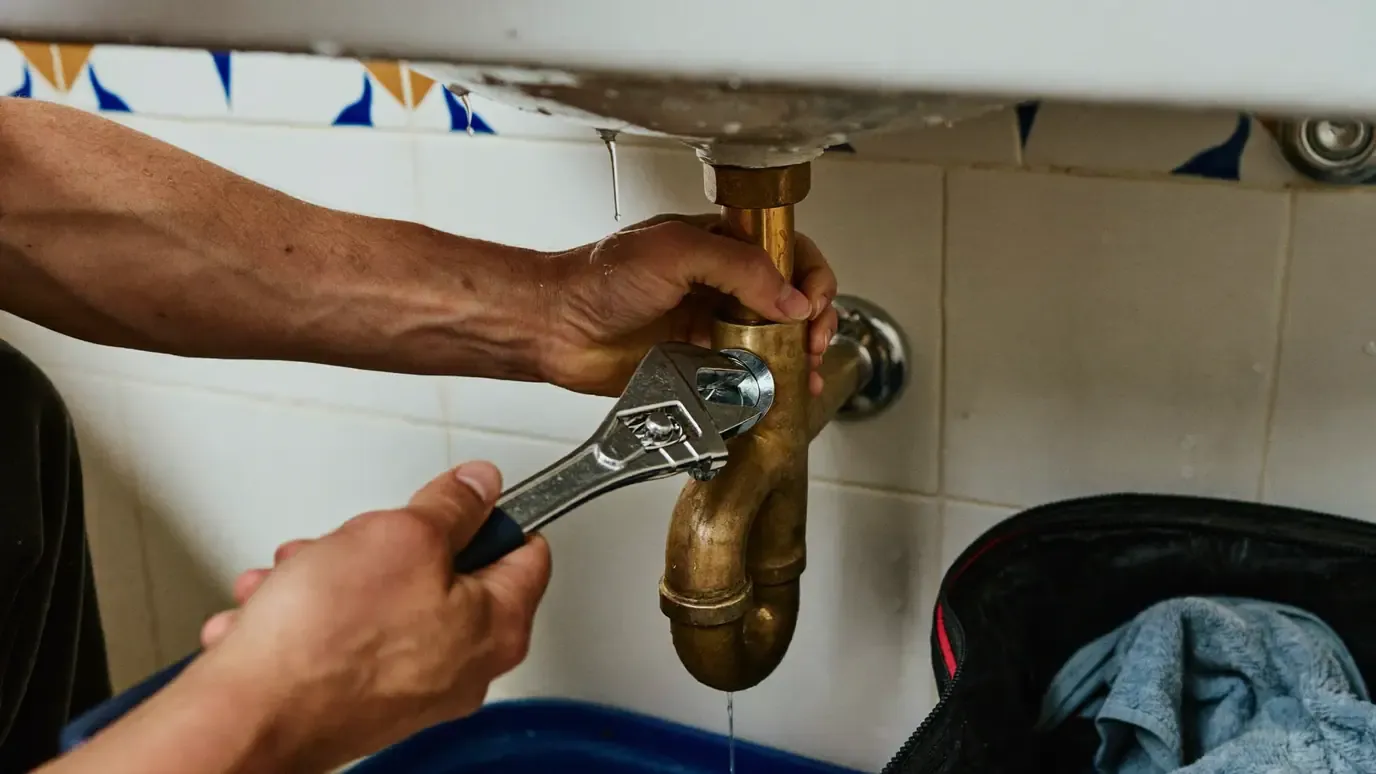 Adjustable wrench being used on the brass trap under a kitchen sink