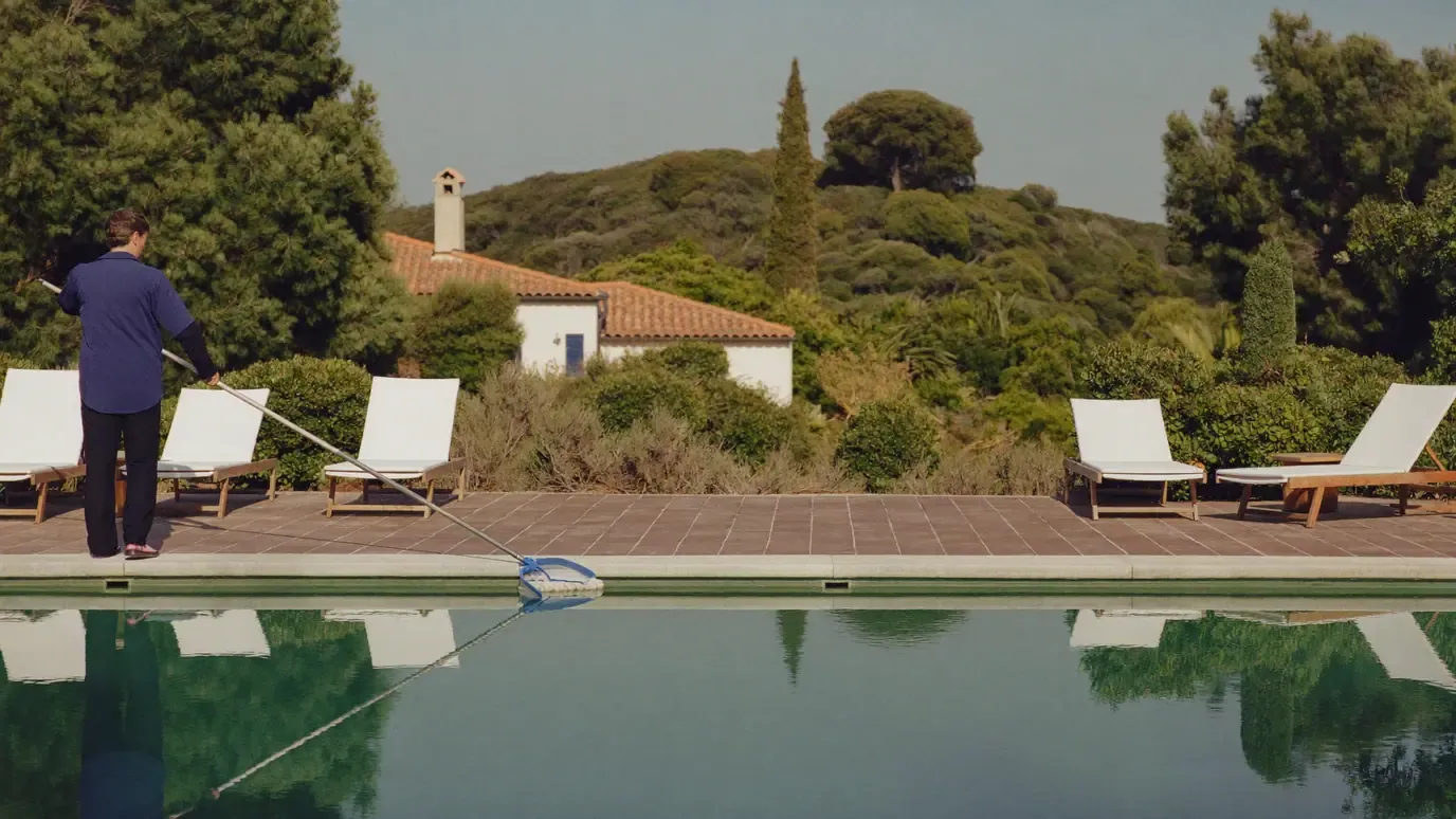 Pool technician skimming the surface of a villa pool with a long handled net