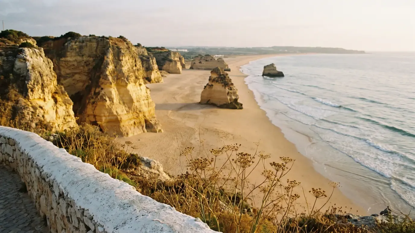 Golden sandstone cliffs and sea stacks above an empty beach at Praia da Rocha, Portimão, seen from the cliff path