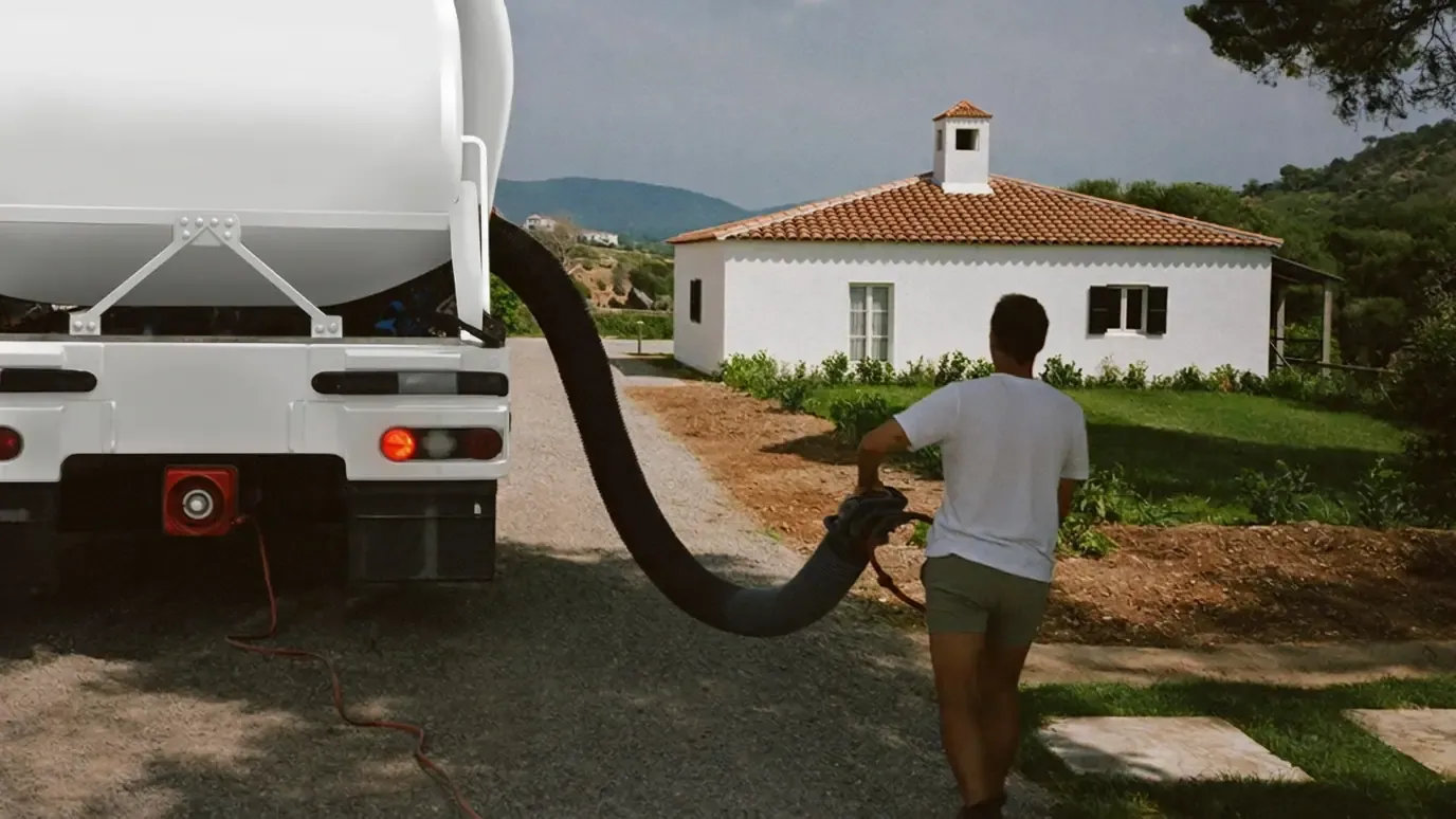 Vacuum tanker parked on a gravel drive with the suction hose run across to a country house