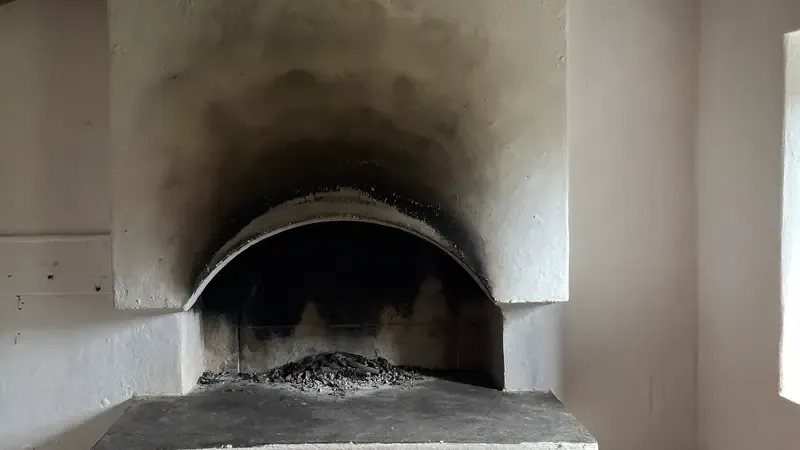 Soot blackened opening of a rustic fireplace with ash on the hearth